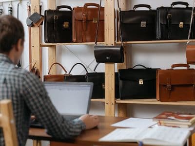 Homme à son bureau devant une collection de cartables et sacoches en cuir